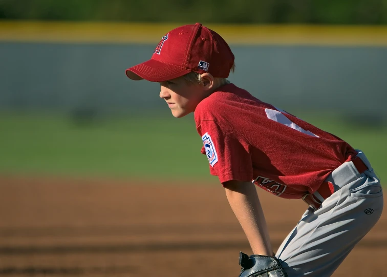 a boy in red baseball uniform bending over a base