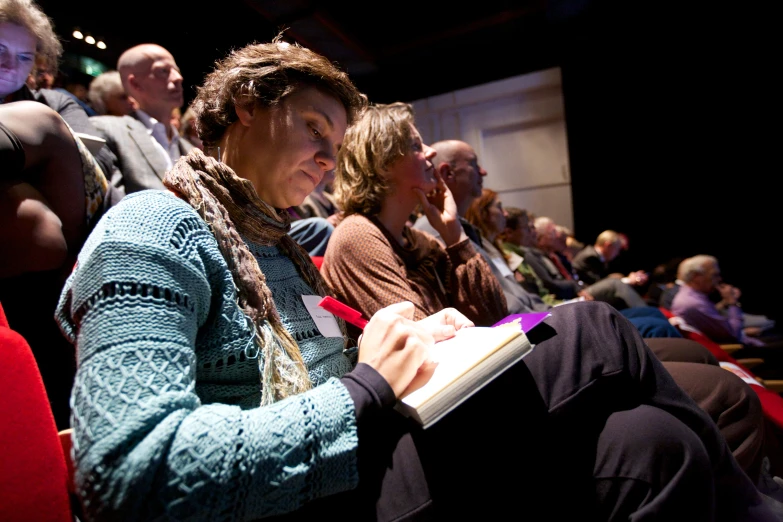 people are seated in rows with notebooks open