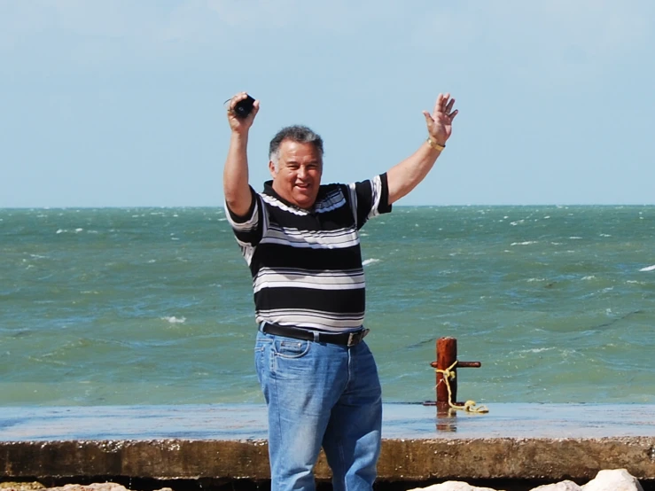 the man holds his arms up while standing on a rock wall overlooking the water