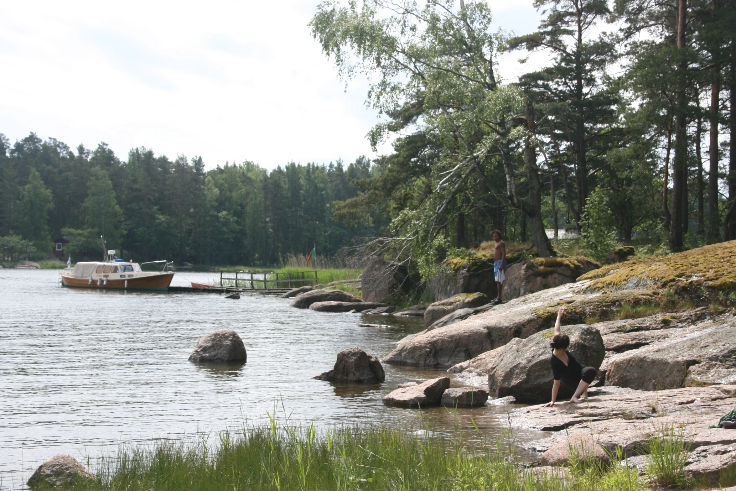 two young people sitting by the water while others stand on the rocks