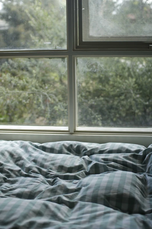 a white bed next to two windows with lots of blankets