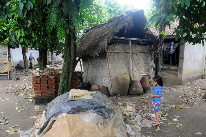 there is a little girl standing in front of a small hut