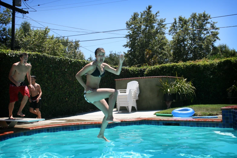 a woman jumping into the pool as people look on
