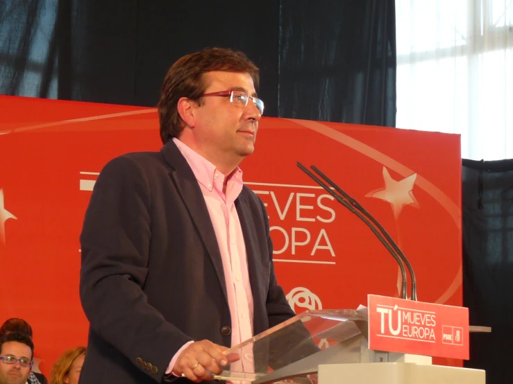 a man with glasses stands behind a podium