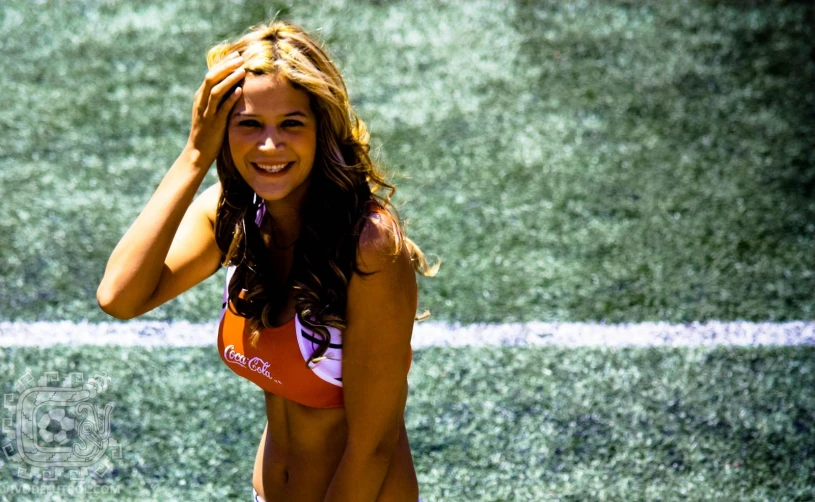 a beautiful woman wearing an orange and white bikini standing on top of a soccer field