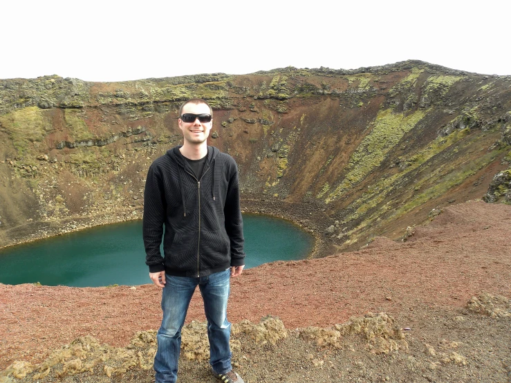 a man in jeans and glasses is standing near a lake