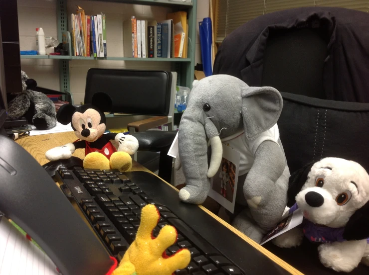 two stuffed animals sit on a desk in front of a computer keyboard