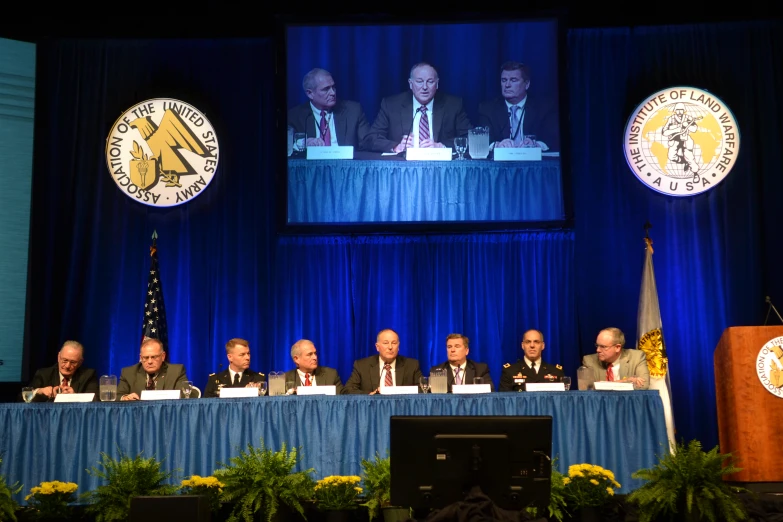 five officials at a table on stage looking at soing in the distance