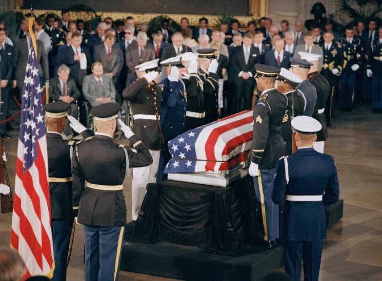 military people and soldiers stand beside an casket