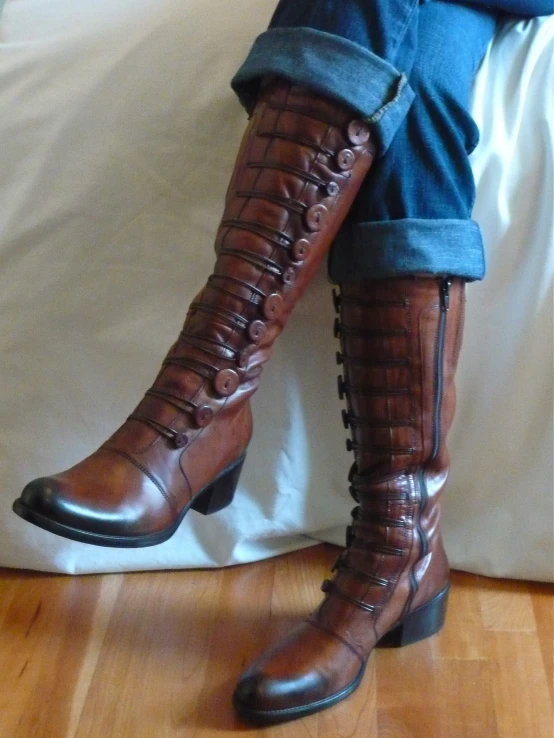 a pair of brown leather boots sitting on top of a bed