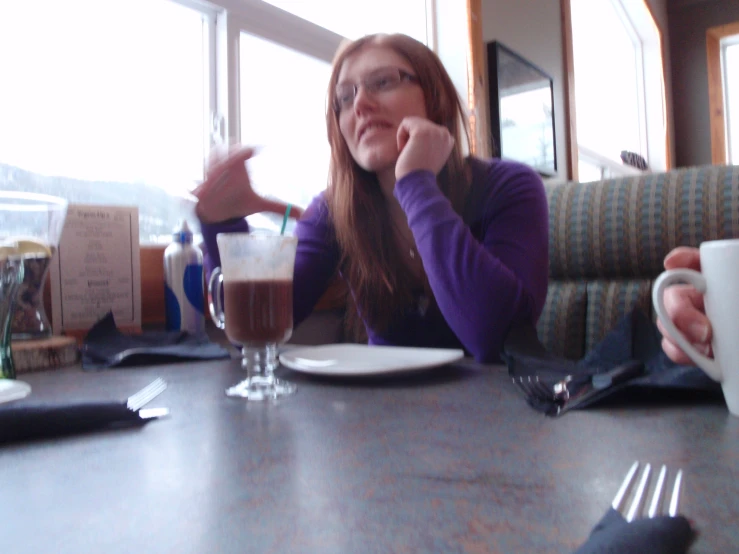 a woman sitting at a table with a glass and two forks in front of her