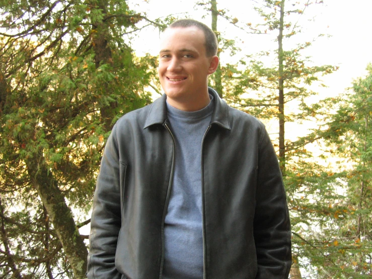 a man in jacket looking forward in front of trees