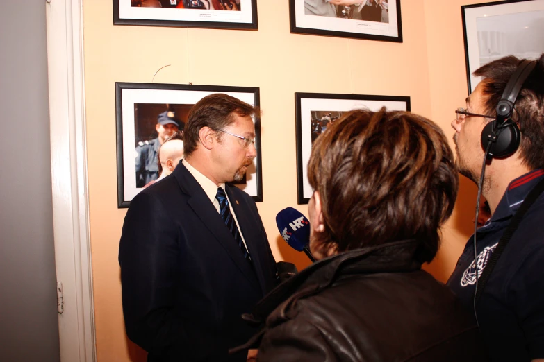 the man is interviewing his radio partner in a room with pictures on the wall