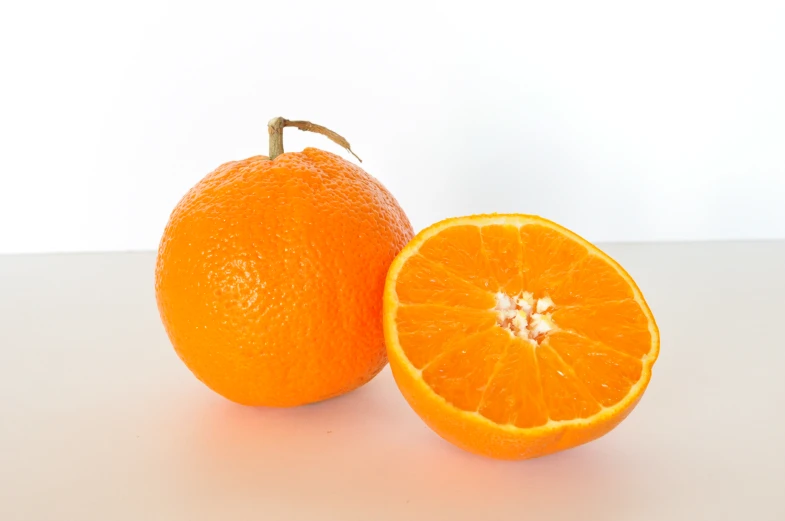 a half and whole orange sitting on a white counter