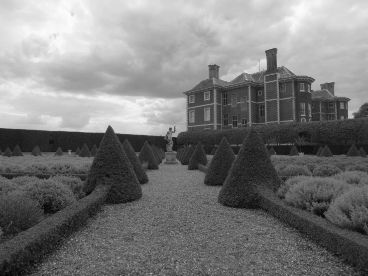 an old brick building sits behind hedges with an empty path leading towards it