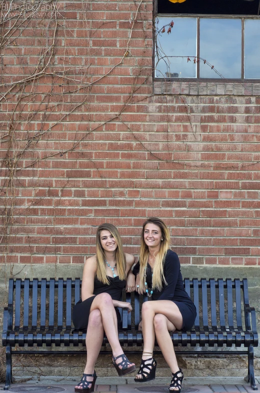 two women are sitting on a bench in front of a building