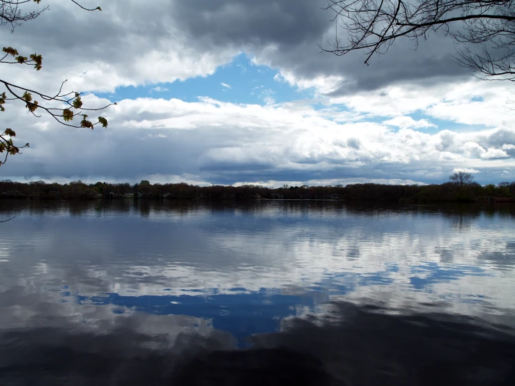 a cloudy day is reflected in the calm water of a lake