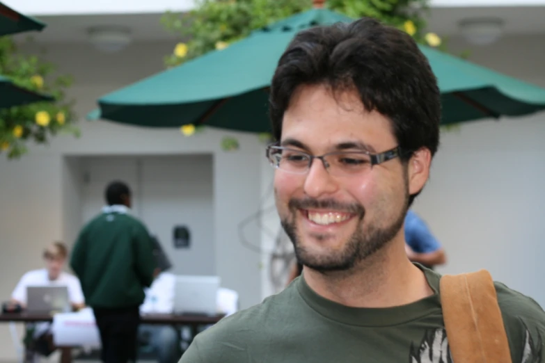 a man that is wearing glasses smiles and holding a bag