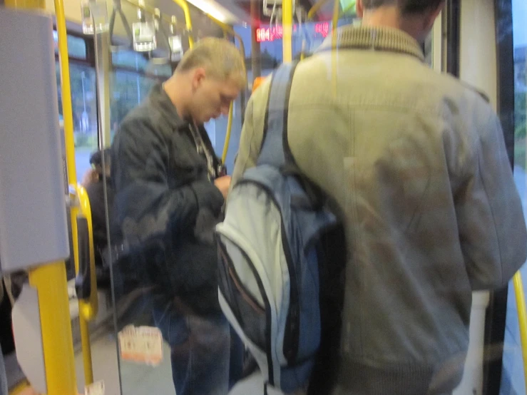 a man looks down as he holds onto a backpack on a subway