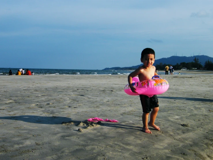 a boy standing on the beach while holding an inflatable ball