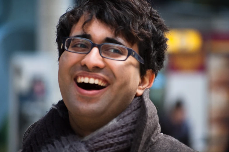 a smiling man wearing glasses, a scarf and a sweater