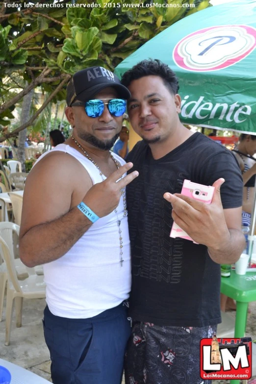 two men wearing sun glasses stand next to each other under a canopy