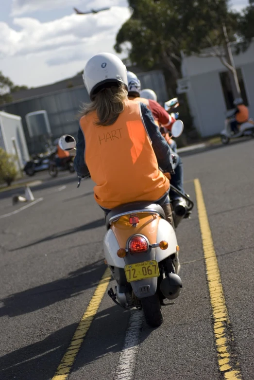 two people riding motorcycles on a street near a parking lot