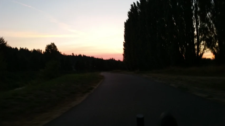 a road with a sunset and some trees near the horizon