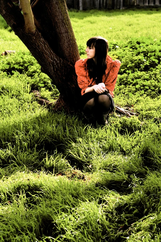 a woman sitting on the ground beneath a tree