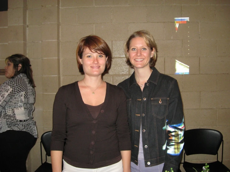 two women posing for the camera in front of a brick wall