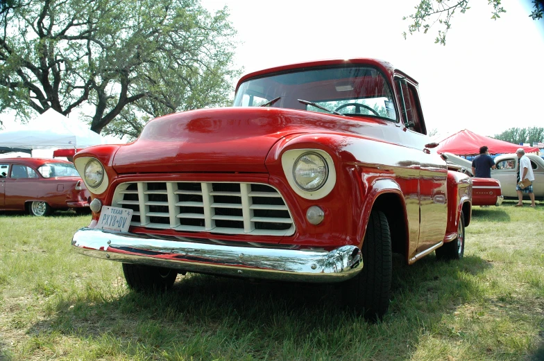 an old red truck parked on the grass near people