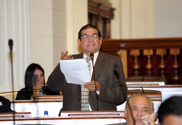 the speaker in a suit standing with his hands up