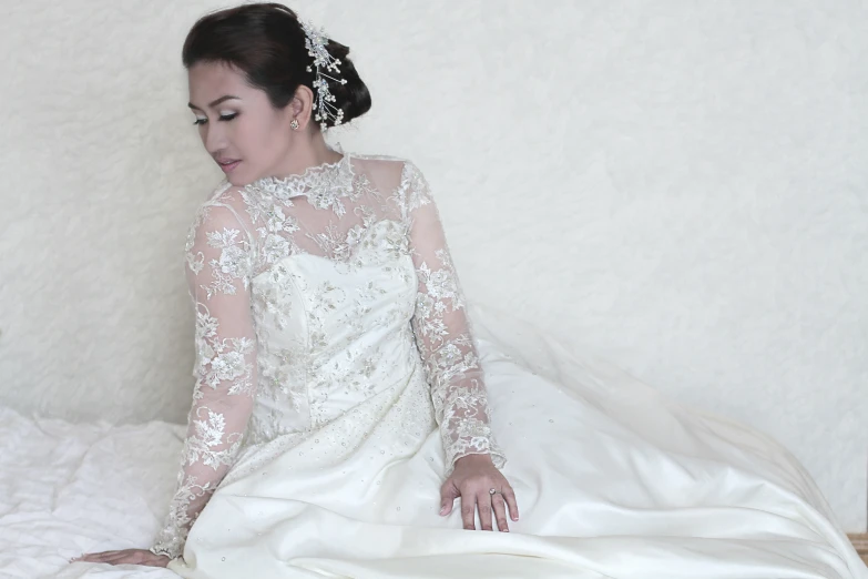 woman in wedding dress sitting on bed in white room