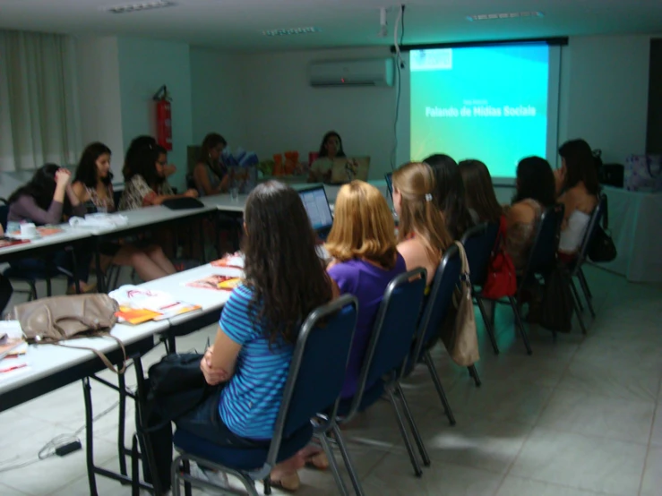 many people sitting at long tables and a projector screen