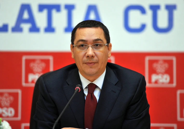 an asian man wearing glasses sits behind a microphone