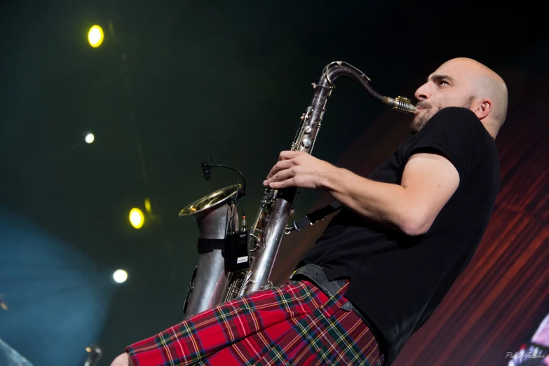 a man in tartan shorts plays the saxophone on stage