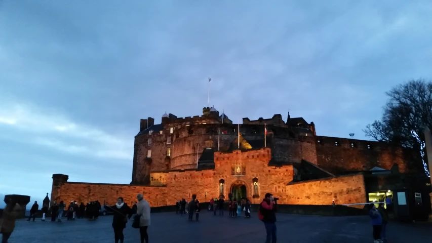 people are standing in front of a castle at twilight