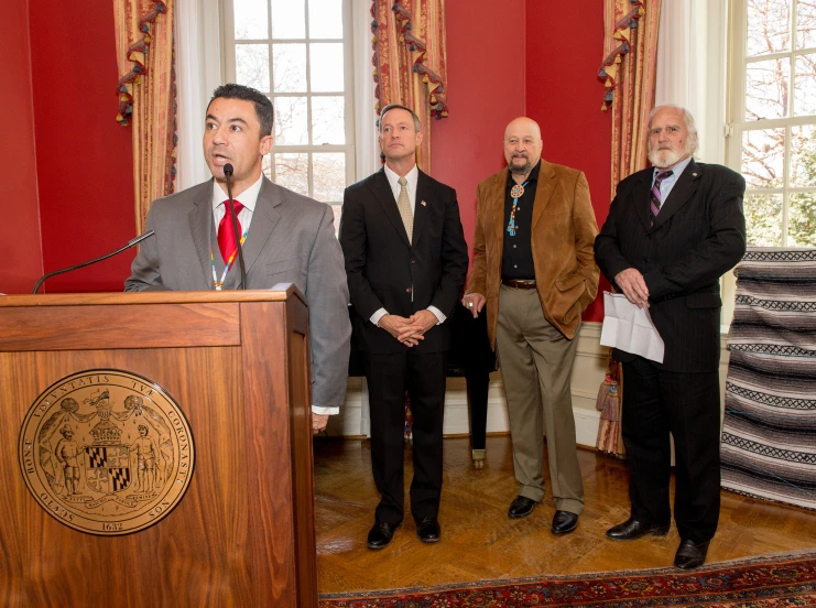 four men in suits standing behind a podium