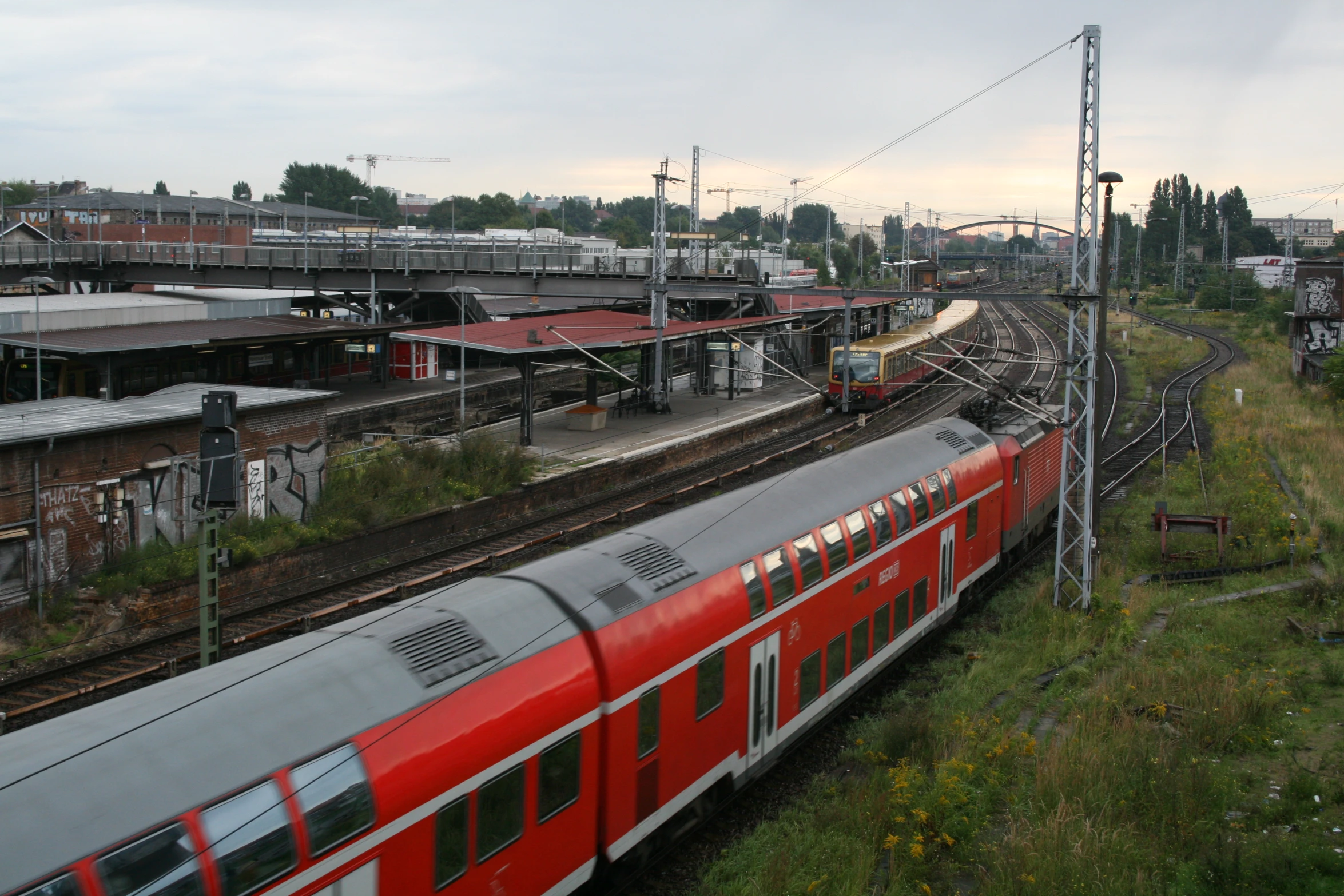 a red train going down the tracks next to buildings