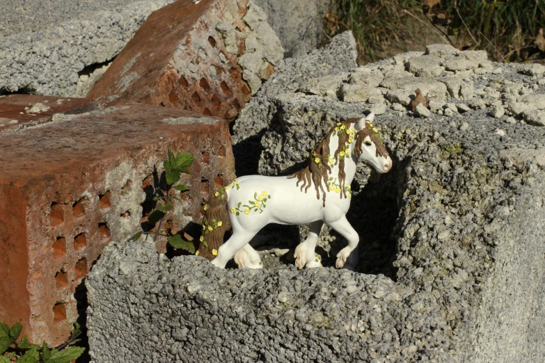 white pony figure in hole in cement wall with flowers