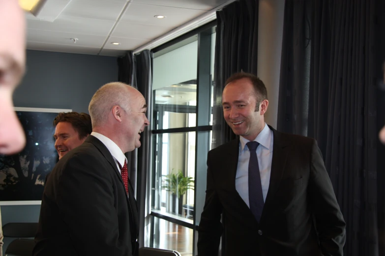 two men in suits are talking and smiling