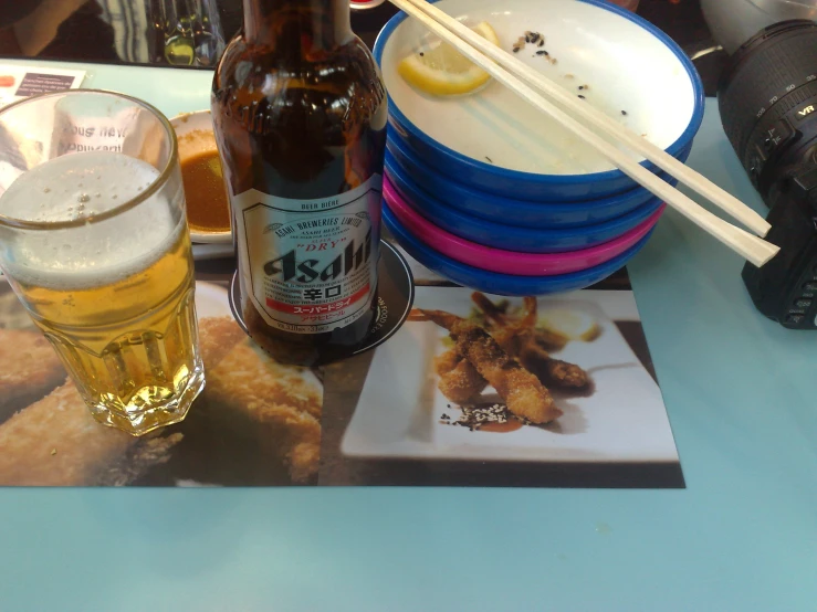 a beer, a plate of food and chopsticks on a table