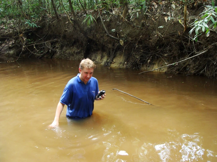 a man holding soing in his right hand and wading through a muddy river