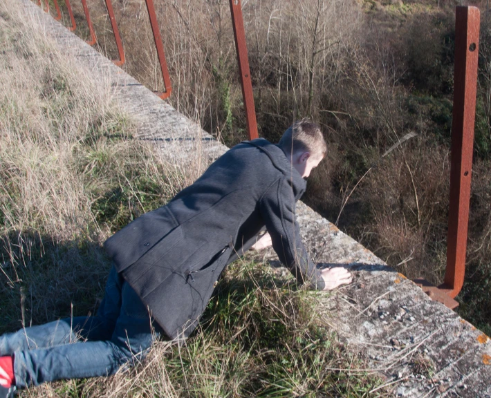 a man in black jacket laying on cement and metal bridge