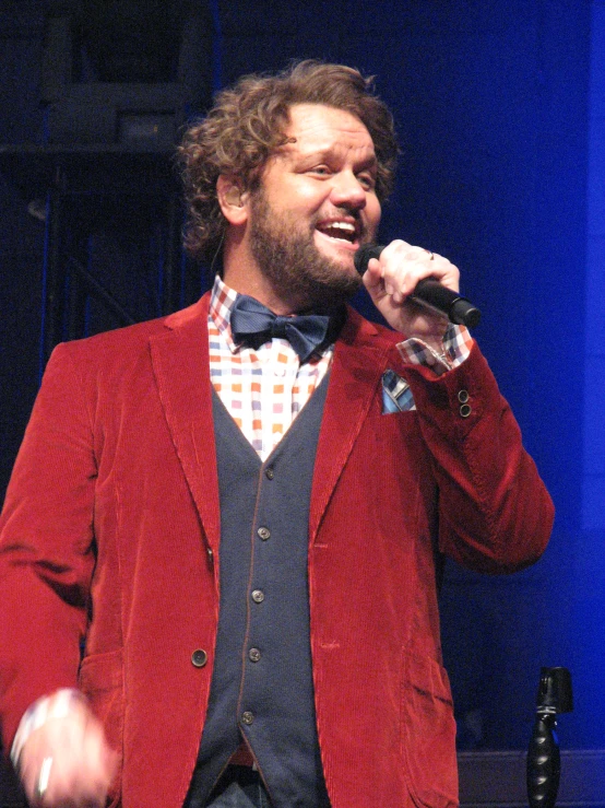 a man in a red jacket and bow tie with a microphone