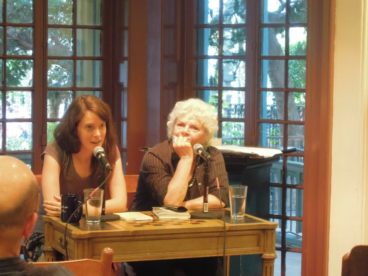 two women sitting in front of microphones at a table with glasses of water