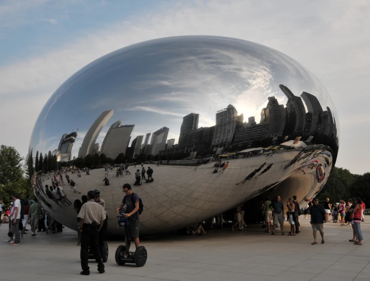 a giant silver ball sits in a crowded area while people walk by