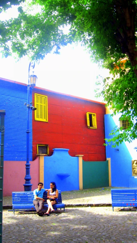 the people are sitting on the blue benches by the street