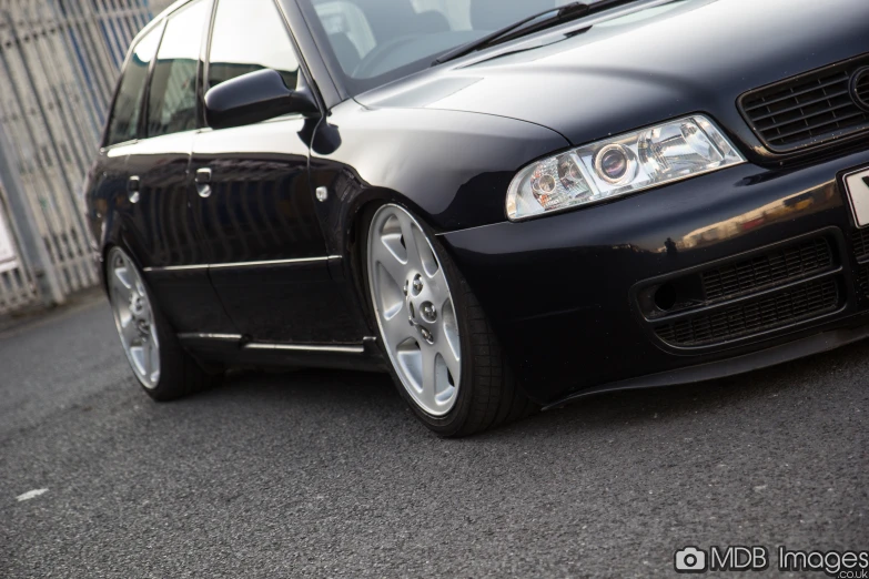 a black car with silver rims is parked by a fence