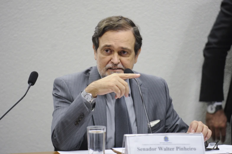 an older man in a business suit with a hand over his mouth at the microphone